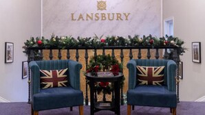 A reception area with a marble wall, two armchairs with Union Jack pillows, a small table with a book, and Christmas decorations.