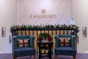 Ein Empfangsbereich mit Marmorwand, zwei Sesseln mit Union-Jack-Kissen, einem kleinen Tisch mit einem Buch und weihnachtlicher Dekoration.