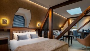 A bedroom with a large bed, a desk, and a chair, with a sloped ceiling and skylight. - Lansbury Studio Suite (London)