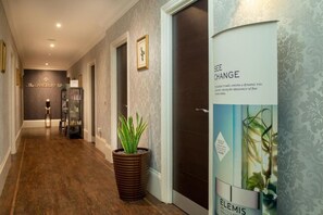 A hallway with a sign for The Lansbury Spa, a potted plant, and a door with a poster advertising ELEMIS. - The Lansbury Heritage By Sunday - Lansbury Studio Suite (London)