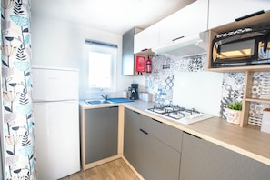 Eine kompakte Küche mit Kühlschrank, Spüle, Herd, Mikrowelle und einem Fenster.