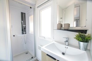 Een badkamer met douche, wastafel, spiegel en een plant in pot.