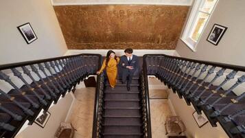 A man and woman on a staircase with a patterned wall and framed pictures.