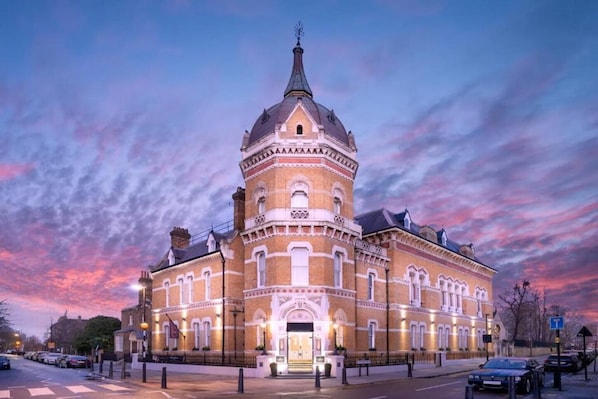 Ein historisches Gebäude mit einem markanten Turm, großen Fenstern und einem gut beleuchteten Eingang.