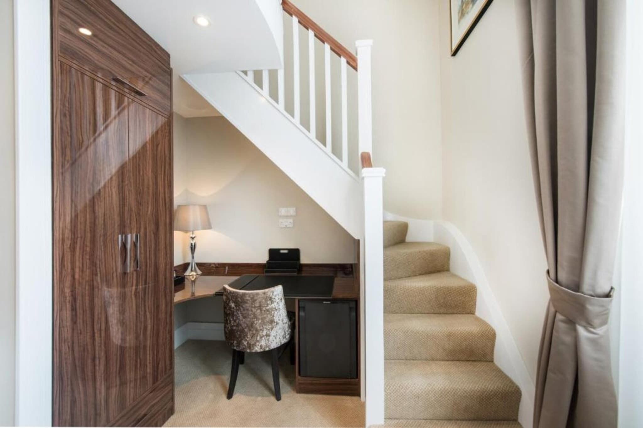 A staircase with a white railing, a desk with a lamp, a small chair, and a cabinet.