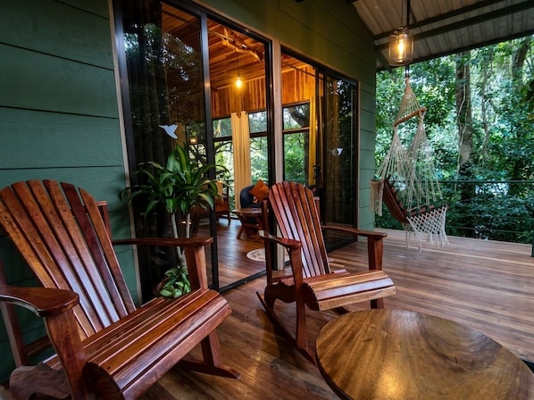 A wooden deck with two Adirondack chairs and a round table, overlooking a lush green forest. - Jungle Living Tree Houses (Monteverde)