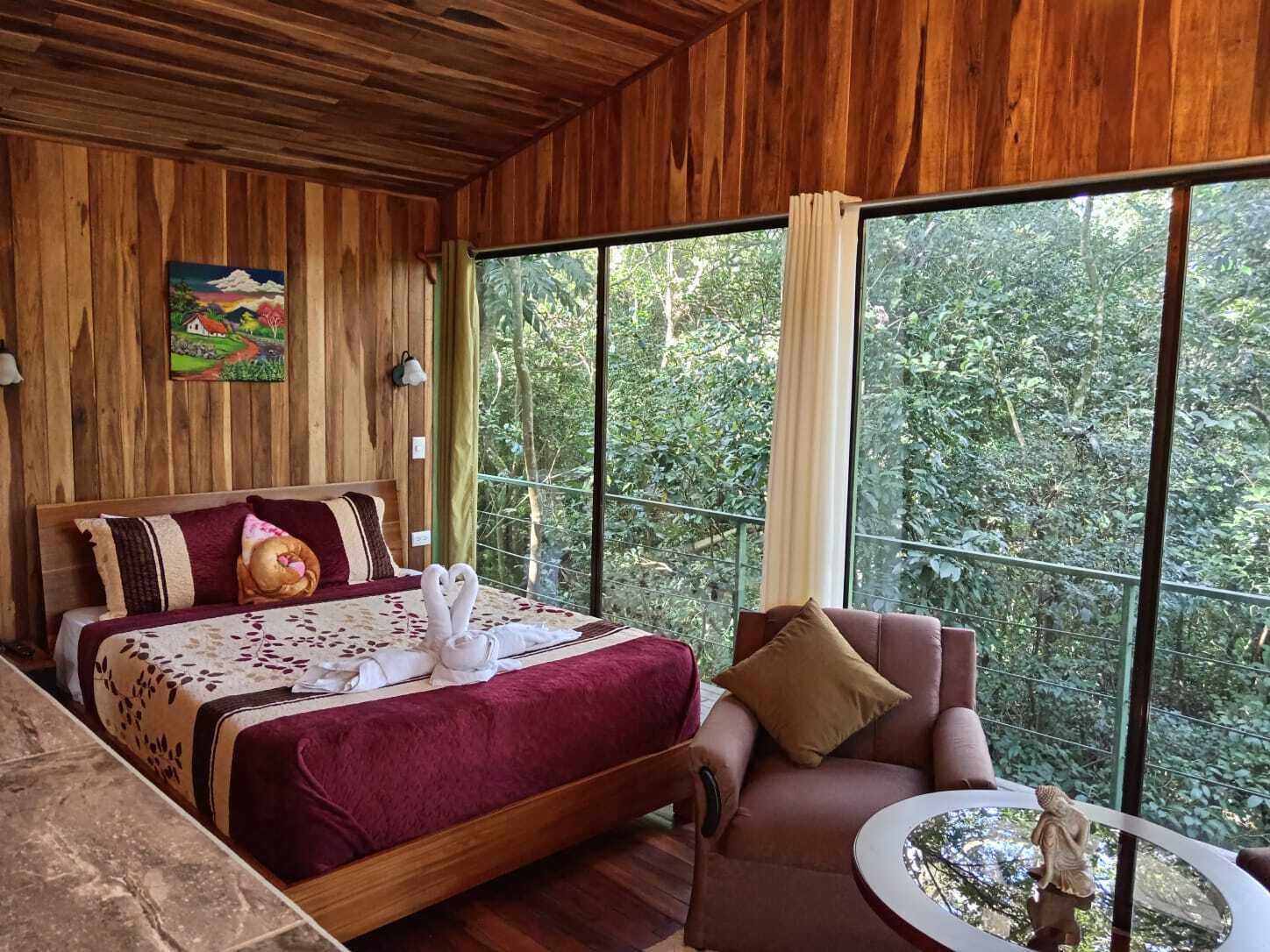 Um quarto de madeira com uma cama, um sofá, uma mesa pequena e um quadro na parede.