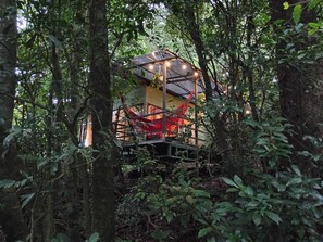Een boomhut met een glazen omheining, omgeven door dicht bos.