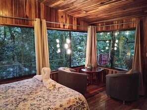 A room with a bed, two chairs, a small table, and large windows with curtains. - Jungle Living Tree Houses (Monteverde)