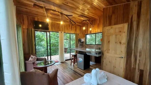 A wooden cabin with a bed, a desk, and a view of the outdoors. - Jungle Living Tree Houses (Monteverde)