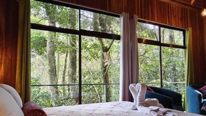 A bedroom with a large window, a bed with white linens, and a blue chair. - Jungle Living Tree Houses (Monteverde)