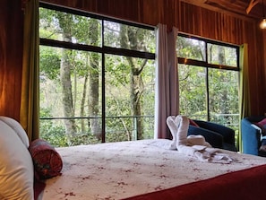 A bedroom with a large window, a bed with white linens, and a blue chair. - Jungle Living Tree Houses (Monteverde)