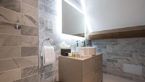 Een badkamer met marmeren tegels, een wastafel met spiegel, een handdoekrek en een prullenbak.