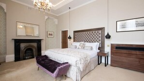 Een slaapkamer met een groot bed, een open haard, een kroonluchter en een ingelijst schilderij aan de muur.