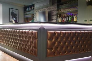 Una zona de bar con un mostrador de cuero capitonado y estantes llenos de botellas.