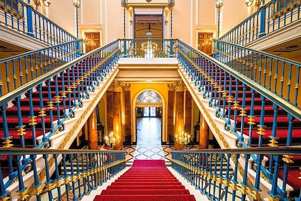 A grand staircase with red carpet and blue railings leading to a central archway.