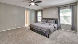 Ein Schlafzimmer mit einem Bett, Deckenventilator und zwei mit Vorhängen versehenen Fenstern.