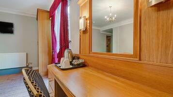 A hotel room with a wooden dresser, a mirror, a chandelier, and a window with curtains.