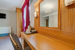 A hotel room with a wooden dresser, a mirror, a chandelier, and a window with curtains.