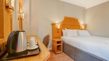 A hotel room with a bed, bedside table, a kettle, a cup, and a tray.
