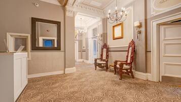 A hallway with ornate wall moldings, a chandelier, and two ornate chairs.