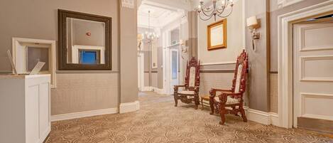 A hallway with ornate wall moldings, a chandelier, and two ornate chairs.