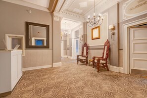 A hallway with ornate wall moldings, a chandelier, and two ornate chairs.