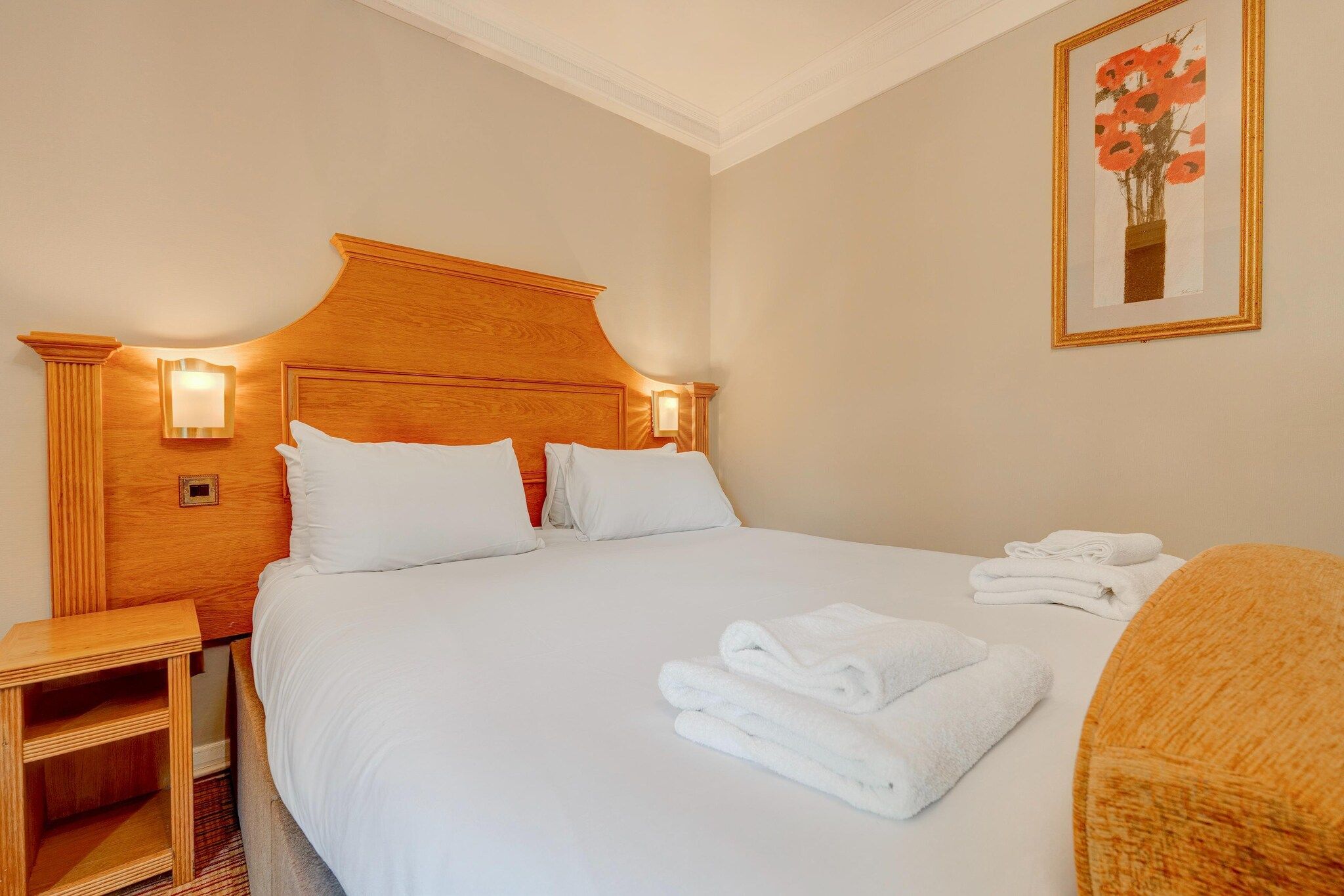 Une chambre d’hôtel avec un grand lit, deux tables de chevet, une petite table et un tableau encadré au mur.