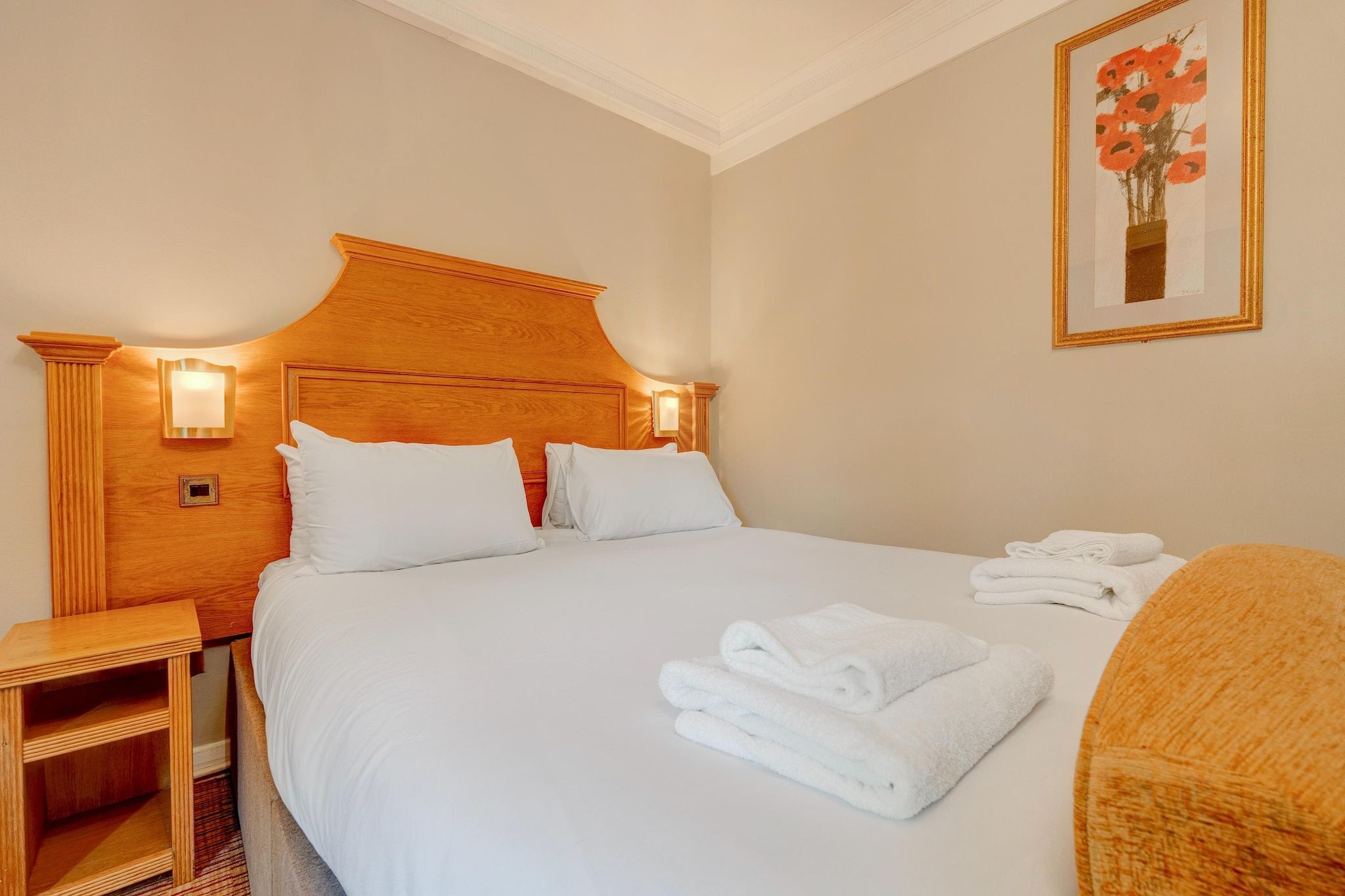 A hotel room with a large bed, two bedside tables, a nightstand, and a framed artwork on the wall.