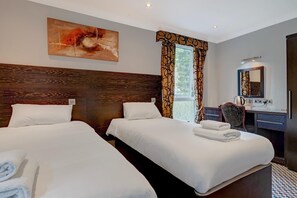 Et hotelværelse med to senge, et skrivebord, en stol, et spejl og et billede på væggen.