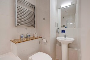 Et badeværelse med toilet, håndvask, håndklædestige og et spejl.