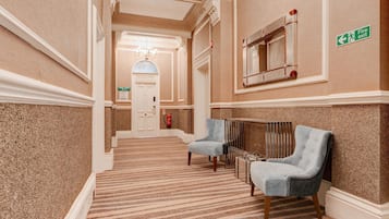 A hotel hallway with a carpeted floor, two armchairs, a fire exit sign, and a door labeled 'The Director's Suite.'