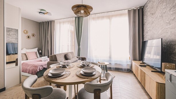 Ein modernes Hotelzimmer mit einem runden Esstisch, einer Couch, einem Fernseher und einem großen Fenster mit Vorhängen.