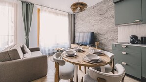 Ein modernes Wohnzimmer mit einer Couch, einem Esstisch, Stühlen, einem Fernseher und einer Küchenzeile mit Schränken und Geräten.