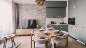 Ein modernes Wohnzimmer mit Essbereich, Fernseher und einer Küche mit grünen Schränken.