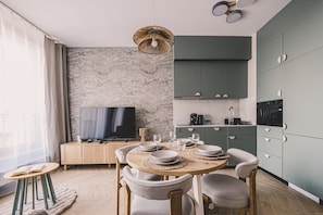 Un salon moderne comprenant un coin repas, un téléviseur et une cuisine avec des meubles de couleur verte.