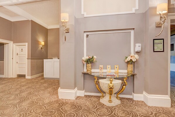 A reception area with a marble console table, two wall-mounted lamps, and a door with a sign indicating payment on arrival.