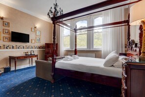 A four-poster bed with a canopy, a television mounted on the wall, and a desk with a chair.