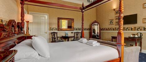 A four-poster bed with a wooden frame, a flat-screen TV mounted on the wall, and a large mirror above the bed.