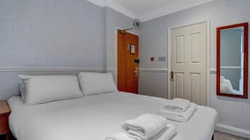A hotel room with a large bed, a wooden door, a mirror, and a wall-mounted light fixture.