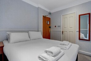A hotel room with a large bed, a wooden door, a mirror, and a wall-mounted light fixture.