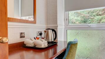 A hotel room with a wooden counter, a kettle, and a tray with cups and utensils.