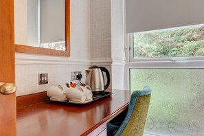 A hotel room with a wooden counter, a kettle, and a tray with cups and utensils.