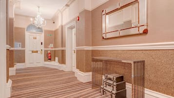 A hotel lobby with a grand staircase, a chandelier, a fire extinguisher, and a mirror on the wall.