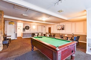 Een biljartkamer met een pooltafel, stoelen en een dartbord.