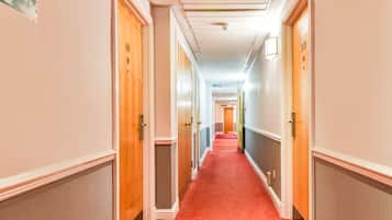 A hotel hallway with a red carpet, wooden doors, and a fire exit sign.