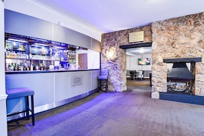 A bar area with a stone wall and a fireplace, bar stools, and a sign indicating hotel amenities. - Accessible Double Room (Derby)