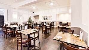 Un grand espace dédié à la salle à manger, avec plusieurs tables et chaises, un sapin de Noël et une grande fenêtre.