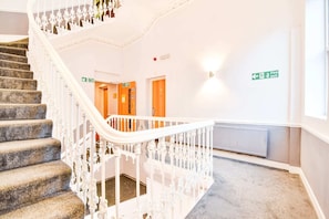 Eine Treppe mit weißer Geländer, Teppichstufen und einer Wand mit einem Brandschutztürschild.