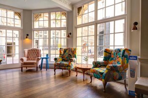 A spacious room with large windows, a classic armchair, colorful armchairs, and a small table. - Bristol Grand By Sunday - Standard Family of 3 Room (Bristol)